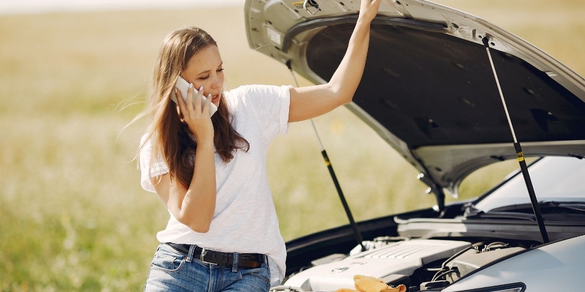 girl on cell phone sitting on hood of her broken down car