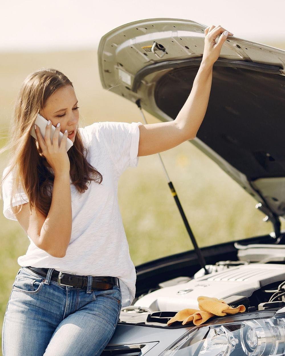 girl on cell phone while sitting on open hood of her car