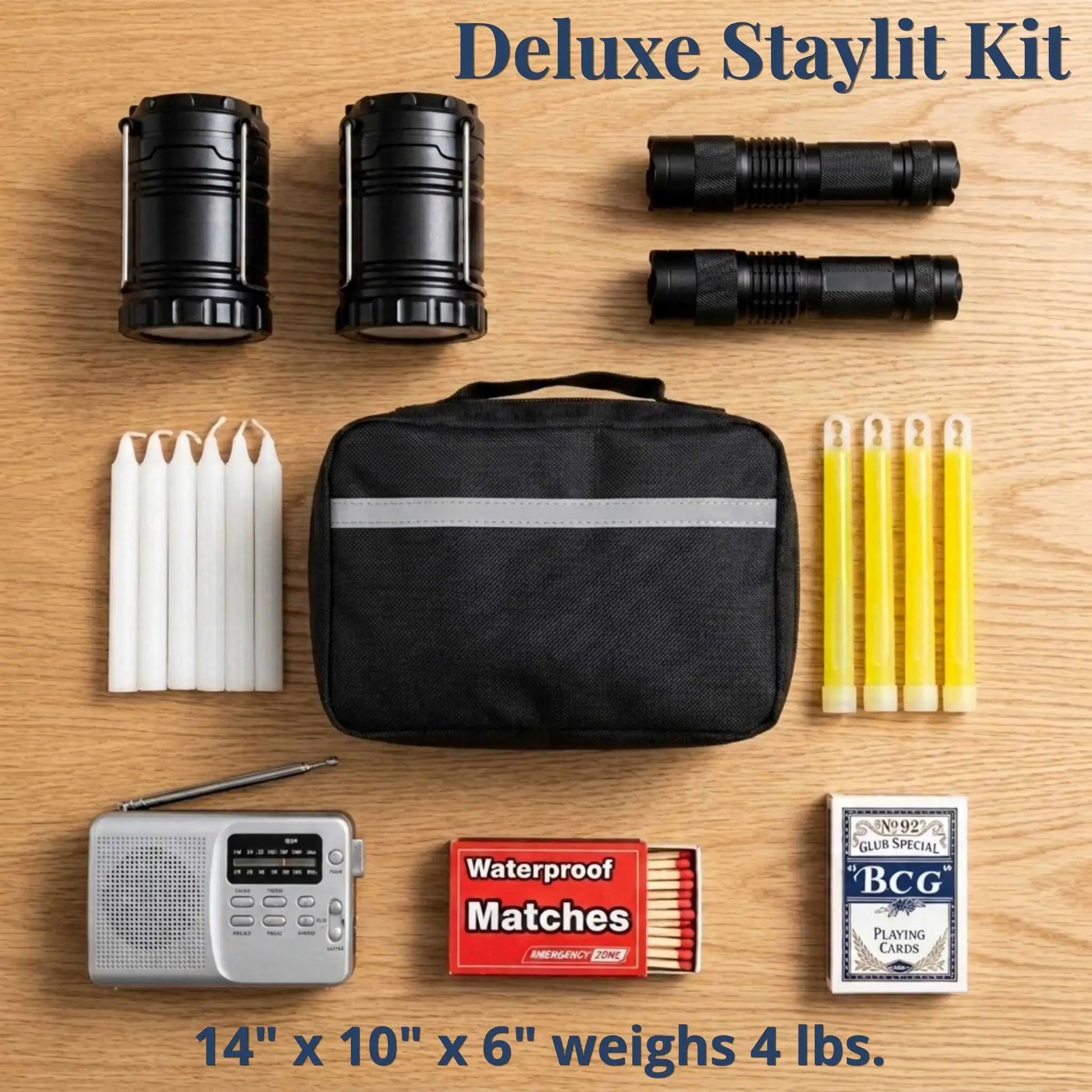 Deluxe Staylit Kit laid out on a light wood background, including two black lanterns, two black flashlights, five white candles, a black zip pouch with a reflective stripe, five yellow pencils, a silver portable radio, red waterproof matches, and a deck of playing cards. Text at the top reads 'Deluxe Staylit Kit' and text at the bottom includes size and weight information.